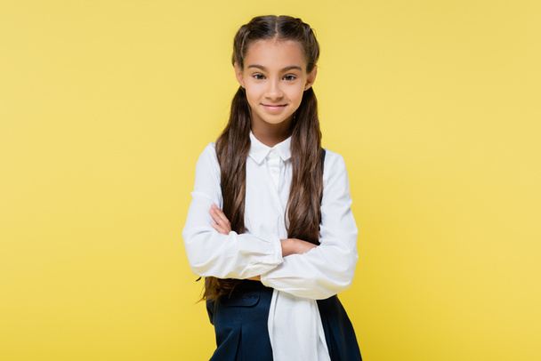 Smiling schoolgirl with crossed arms looking at camera isolated on yellow - Fotografie, Obrázek