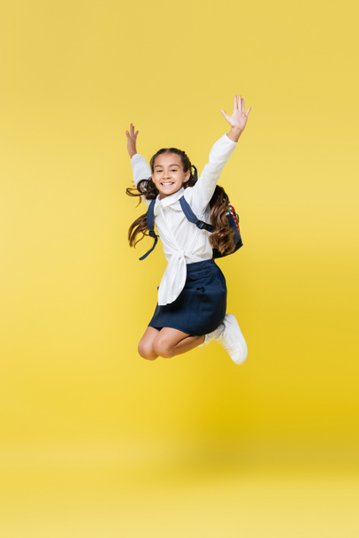 Positive schoolkid jumping and looking at camera on yellow - Фото, изображение