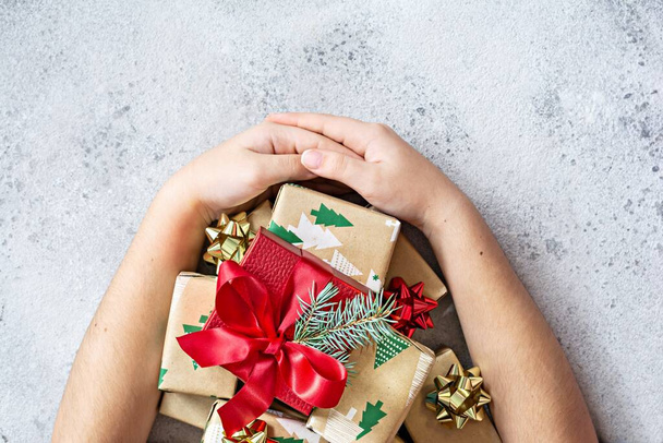 Kezek egy lány ölelés sok kis ajándékokat egy nagy piros doboz közepén, csomagolva ünnepi papír egy fehér (szürke) háttér. Ajándékok karácsonyra és újévre. Ünnepi koncepció, felülnézet, másolás - Fotó, kép