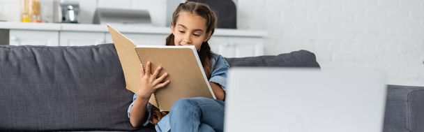 Child holding notebook near blurred laptop at home, banner  - Photo, Image