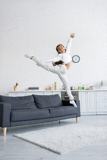 Happy preteen child jumping near couch in kitchen  - Foto, afbeelding