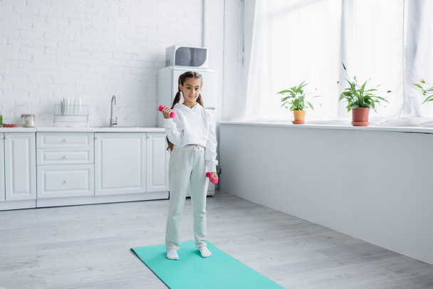 Preteen girl exercising with dumbbells in kitchen  - Foto, immagini