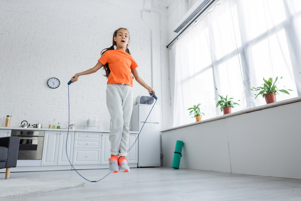 Low angle view of kid jumping with skipping rope in kitchen  - Photo, Image