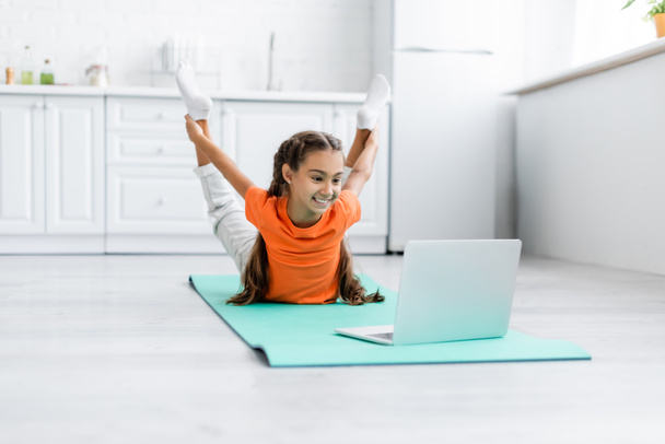 Smiling girl training near laptop on fitness mat at home  - Photo, Image