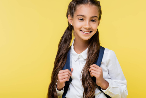 Happy kid in shirt holding backpack and looking at camera isolated on yellow  - Foto, Bild