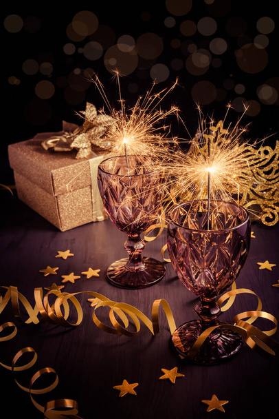 Oudejaarsavond home setting tafel met sterretjes in wijnglas met geschenkdoos en carnaval masker - Foto, afbeelding