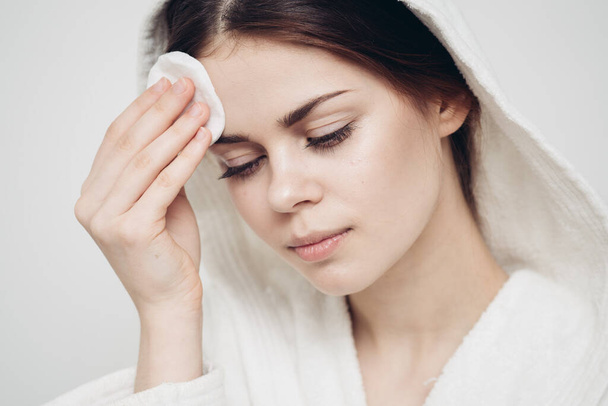 woman with a hood on her head wipes her face with a cotton pad skin care - Photo, Image