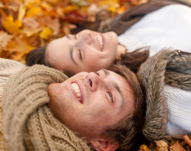 close up of smiling couple lying in autumn park - Foto, afbeelding