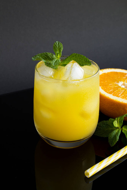 Close-up on orange juice with ice in the drinking glass on the black background. Copy space. Location vertical. - 写真・画像