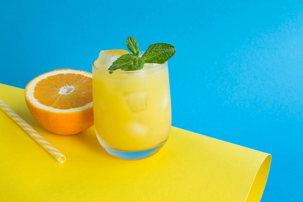 Close-up on orange juice with ice in the drinking glass on the colored background. Copy space. - Photo, Image