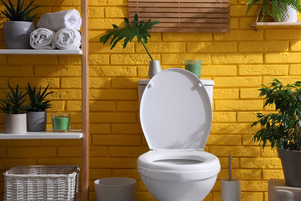 Stylish bathroom with toilet bowl and green plants near yellow brick wall. Interior design - Photo, Image