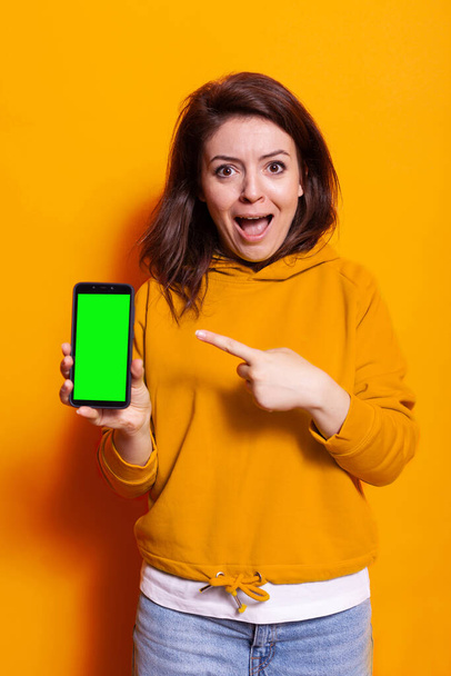 Junge Frau zeigt auf vertikalen grünen Bildschirm auf Smartphone - Foto, Bild