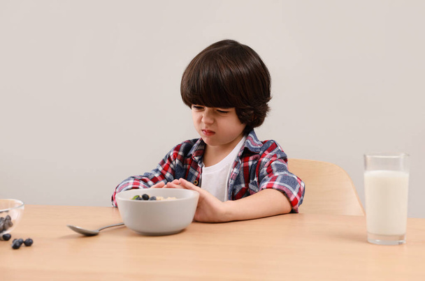 Cute little boy refusing to eat his breakfast at table on grey background - Фото, зображення