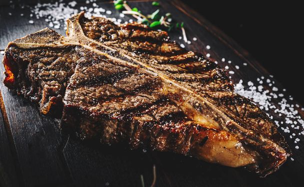 Grilled T-bone Steak on bones on wooden board on dark background - Photo, image