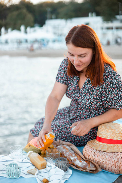 Nuori onnellinen kaunis nainen istuu laiturilla merellä. Piknik meren tai meren rannalla aurinkoisessa auringonlaskussa. Loma - Valokuva, kuva