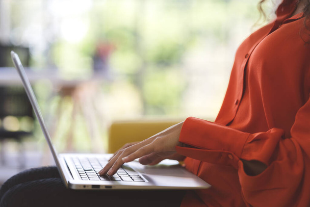 Gros plan jeune femme noire portant une chemise orange à l'aide d'un ordinateur portable pour faire du shopping en ligne, se pencher en ligne, et appel vidéo sur le canapé à la maison. Femme d'affaires travail de la maison dans la propagation du coronavirus covid-19. - Photo, image