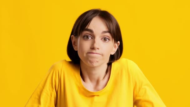 Nieświadoma młoda kobieta robi ramiona ramiona na żółtym tle - Materiał filmowy, wideo