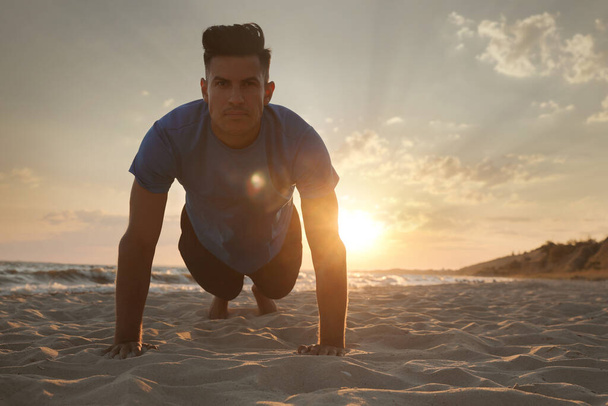 Sporty man doing plank on sandy beach at sunset - Foto, imagen