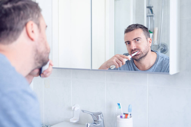 Man die tanden poetst met een elektrische tandenborstel - Foto, afbeelding