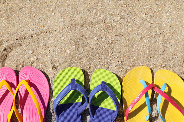 Many different flip flops on sand, flat lay. Space for text - Foto, imagen