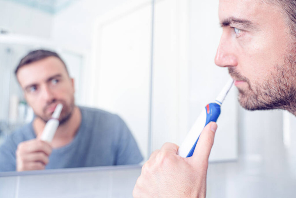 電動歯ブラシで歯を掃除する男 - 写真・画像