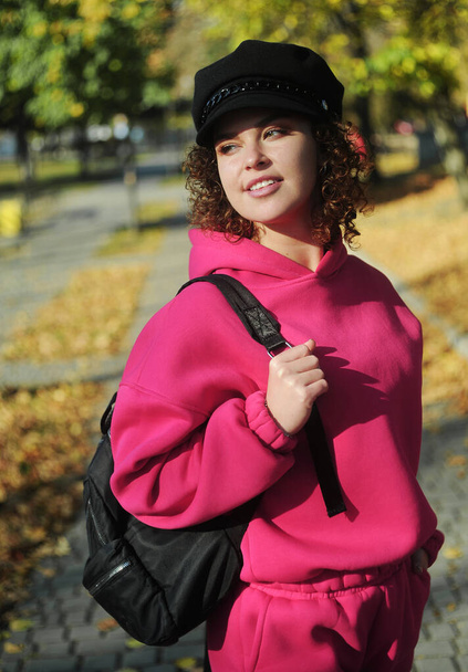 Beautiful woman holding mobile phone in hands outdoors. Curly hair young woman in magenta sporty wear messaging outside - Φωτογραφία, εικόνα