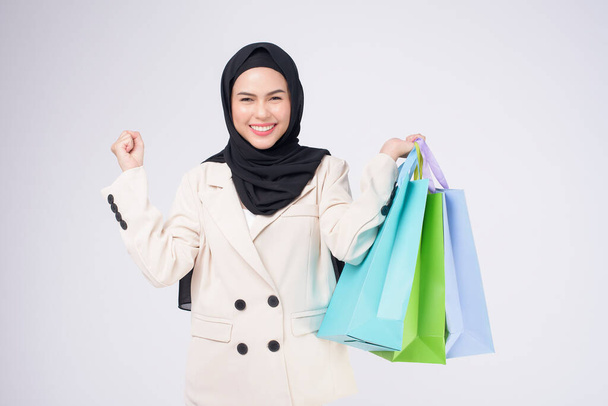 Fiatal gyönyörű muszlim nő öltönyben kezében színes bevásárló táskák felett fehér háttér stúdió - Fotó, kép