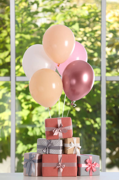 Bunch van kleur ballonnen en prachtig verpakt geschenkdozen op witte tafel in de buurt venster - Foto, afbeelding