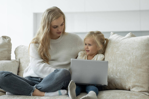 Feliz madre soltera riendo y una linda hija preescolar utilizar una aplicación de computadora portátil en línea, mamá le enseña a una niña cómo usar una computadora - Foto, Imagen