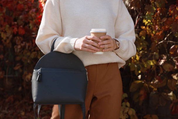 Young woman with stylish grey backpack and hot drink in autumn park, closeup - Фото, зображення