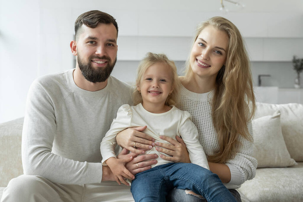 Beautiful young cheerful family is sitting at home on the couch, laughing and playing with each other. - Valokuva, kuva