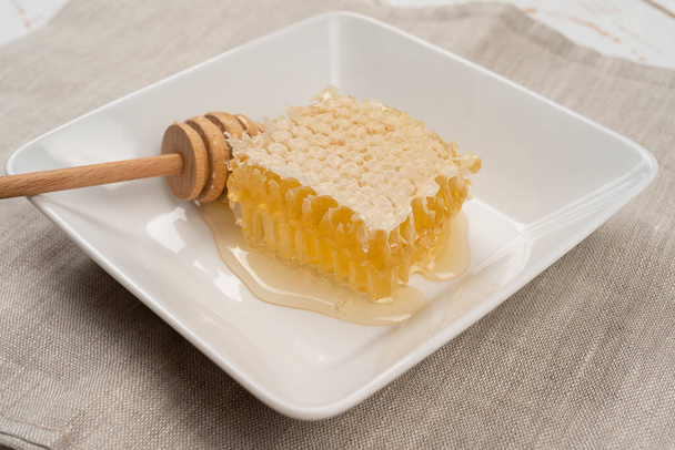 fresh cut golden comb honey slices and natural wooden dipper on plate, isolated on linen background. high angle view - Foto, imagen