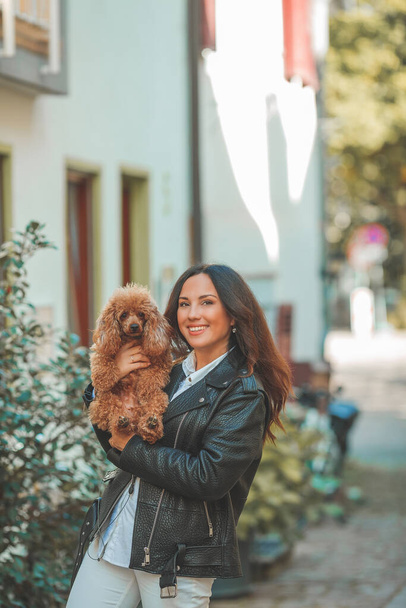 A young beautiful woman with her poodle dog is walking in a European city. Happiness. Little pet. Fall. - Foto, Imagem