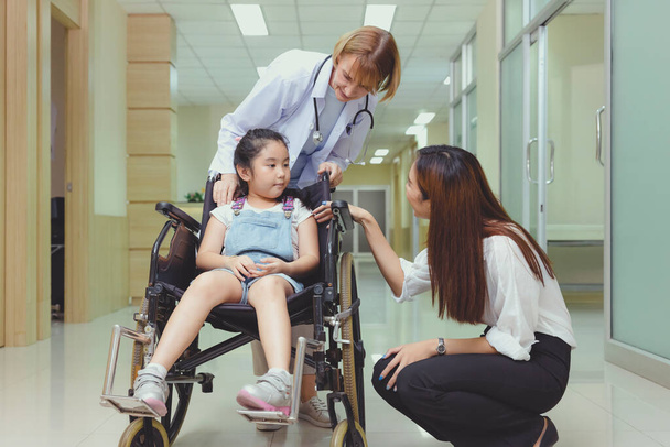 Alors que le médecin vient la voir, une jeune patiente asiatique sourit dans son fauteuil roulant. - Photo, image