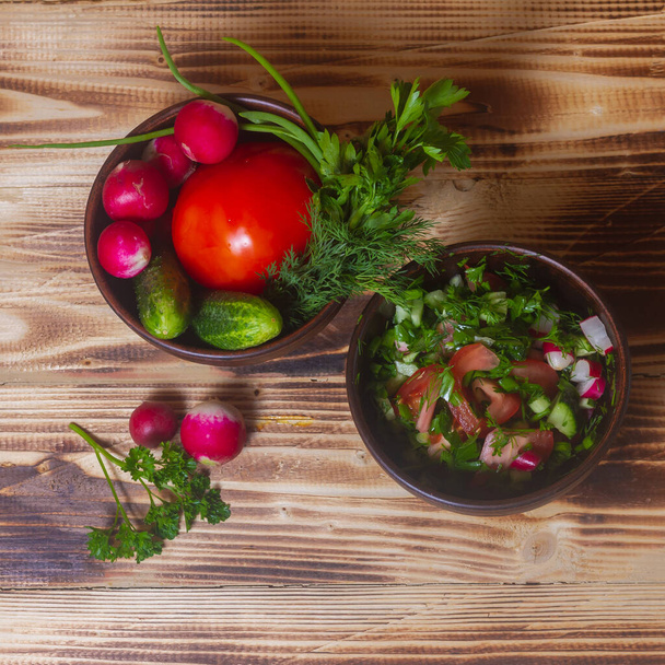 Ingredients for a salad of fresh vegetables, tomatoes, cucumber, dill, rook, radish on a wooden table. - Fotó, kép