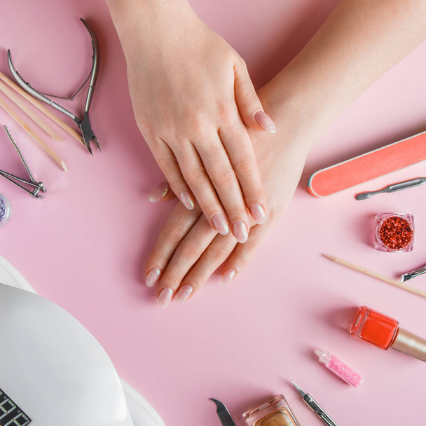 Nail care procedure in a beauty salon. Female hands and tools for manicure on pink background. Concept spa bodycare. - Photo, Image