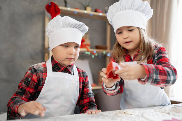 Boy and girl bakers cutting out Christmas cookies with a mold, making gingerbread Christmas tree on the table, children cooking on Christmas eve, close-up. - Фото, изображение