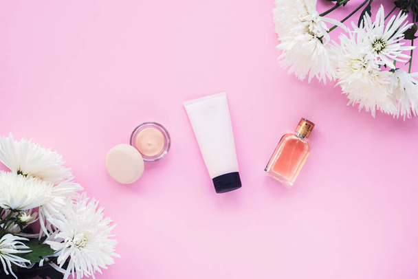Foundation in a jar, cream tube and perfume bottle on pink background with chrysanthemum flowers. Beauty, make up cosmetics concept. Top view, flat lay. - Photo, Image