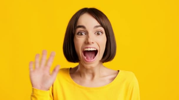Vreugdevolle Millennial vrouw zwaaiende hand Gesturing Hallo over gele achtergrond - Video