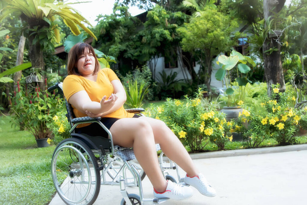 Vette vrouw zat op een rolstoel omdat ze verlamd was, zwakke ledematen, knikte rechterhand en in de tuin om te ontspannen: Verlamming Patiënt Gezondheidszorg Concept - Foto, afbeelding
