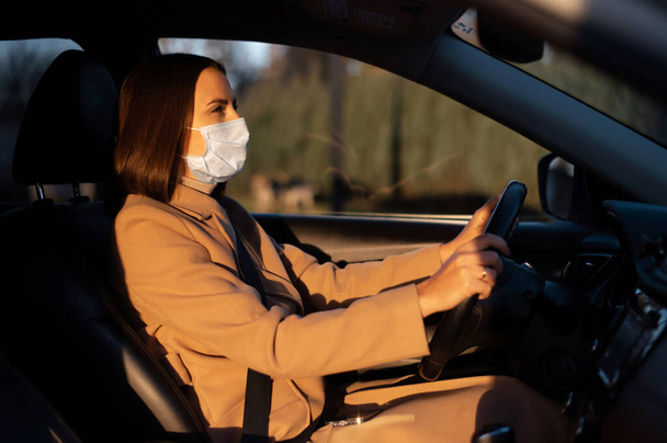 Young woman in smart casual in protective medical mask driving a car - Photo, Image
