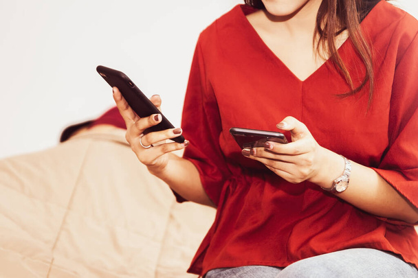 Käsitys perheongelmista: Nuori nainen käyttää kahta puhelinta samaan aikaan makuuhuoneessaan etsimään salaisuuksia ja epäilemään jotain: Valikoiva Focus  - Valokuva, kuva