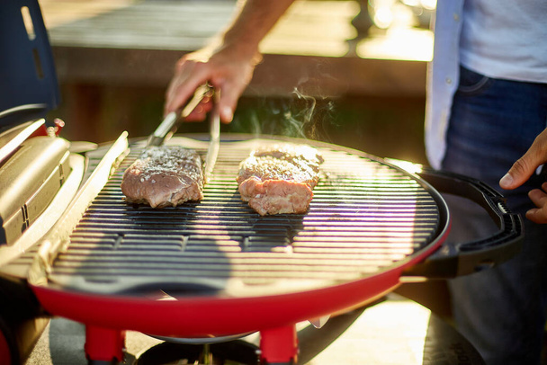 Uomo arrosto di carne alla griglia a gas sul barbecue all'aperto nel cortile, carne alla griglia, picnic estivo in famiglia, cibo sulla natura. - Foto, immagini