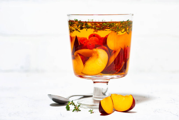flavored black tea with fresh plums, berries and thyme in glass on white background, closeup - Foto, Imagen