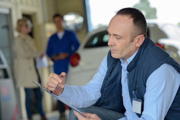 mechanic with clipboard customer waiting in background - Φωτογραφία, εικόνα