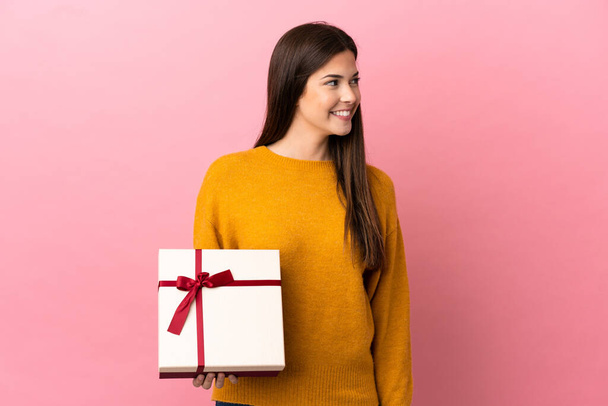 Teenager Brazilian girl holding a gift over isolated pink background looking side - Photo, image