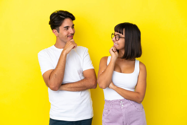 Young mixed race couple isolated on yellow background looking looking at each other - Photo, Image