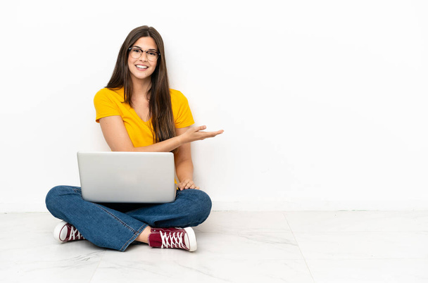 Молода жінка з ноутбуком сидить на підлозі, представляючи ідею, дивлячись посміхаючись до
 - Фото, зображення