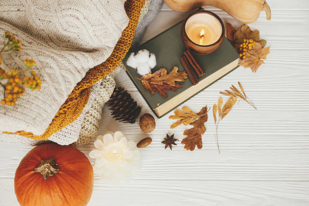 Autumn flat lay. Pumpkin, cozy sweaters, autumn leaves, burning candle and vintage book on white wooden background in room. Hello autumn, cozy slow living.  Happy Thanksgiving - Foto, Imagen