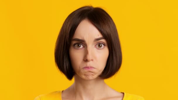 Mujer joven trastornada reteniendo lágrimas posando sobre fondo amarillo - Imágenes, Vídeo